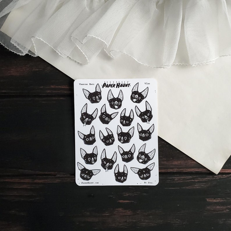 May include: A sheet of stickers featuring 16 black and white illustrations of vampire bats with different expressions. The stickers are on a white background and have the text "Vampire Bats" and "Paper Haunt" printed on them.
