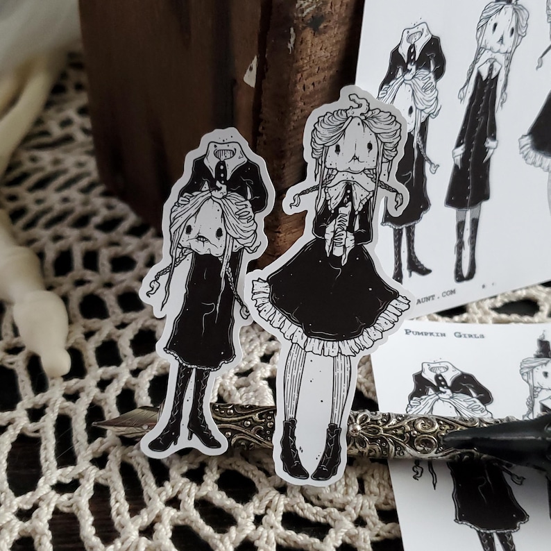 May include: Two black and white illustrations of girls with pumpkin heads. The girls are wearing dresses and have long hair. The text "Pumpkin Girls" is visible in the image.