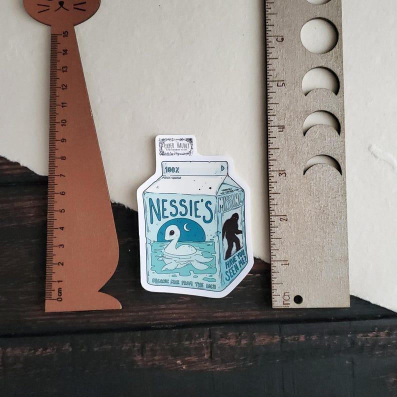 K&ouml;nnte beinhalten: Ein blauer und wei&szlig;er Aufkleber mit einem Cartoon-Milchkarton mit dem Text "Nessie's" und "Have you seen Pie?" Der Karton zeigt ein Loch-Ness-Monster und ein kleines Nessie auf der Vorderseite.