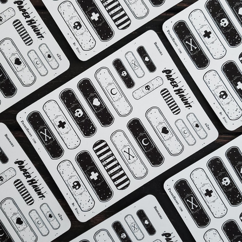 May include: A sheet of black and white band-aid stickers with various designs, including a skull, crossbones, heart, crescent moon, and stripes. The stickers are labeled "Bandages" and "Paper Haunt".