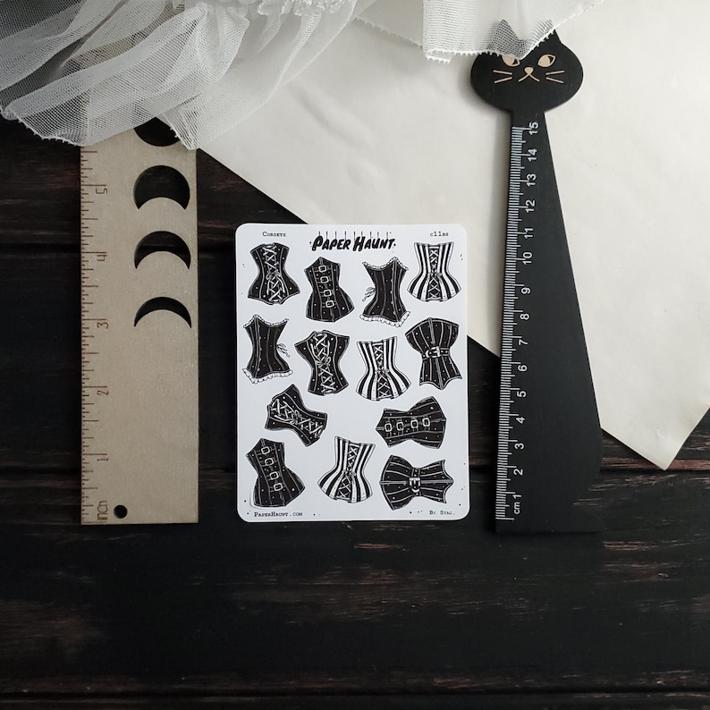 May include: A sheet of black and white stickers featuring a variety of corset designs. The stickers are printed with the text "PAPER HAUNT" and "Corsets".