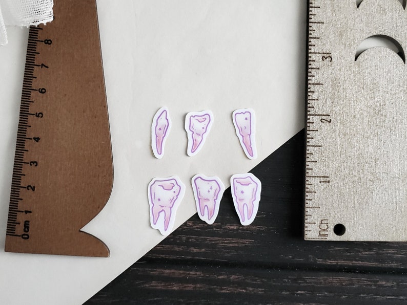 May include: Five pink and white tooth stickers with a glittery design. The stickers are on a white surface.