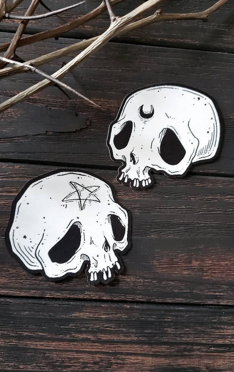 Op de afbeelding: Twee zwart-witte schedelpatches met geborduurde details. De ene schedel heeft een halve maan boven zijn oog en de andere heeft een pentagram op zijn voorhoofd.