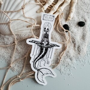 Spooky cute goth Jelly bones mermaid skeleton emerging from water, a sticker Featuring a Mermaid with Translucent skin with visible skeleton and organs with a sea shell on sand.