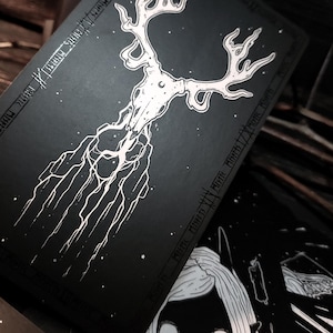 May include: Black and white illustration of a deer skull with antlers, surrounded by a starry sky. The skull is connected to a network of roots and branches, creating a mystical and ethereal design.