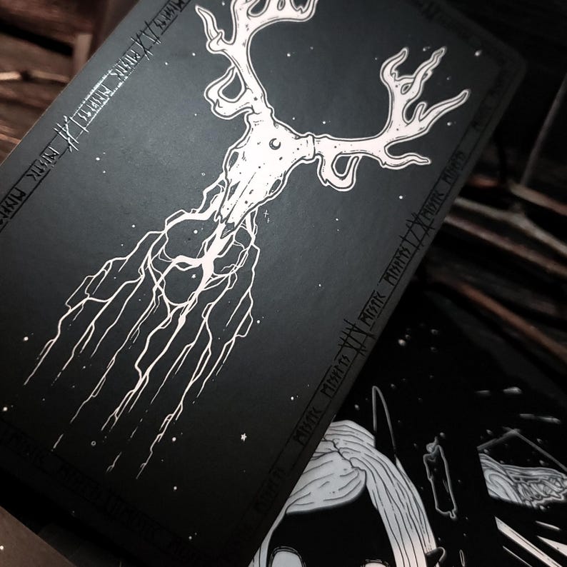 May include: Black and white illustration of a deer skull with antlers, surrounded by a starry sky. The skull is connected to a network of roots and branches, creating a mystical and ethereal design.