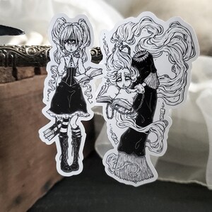 May include: Two black and white illustrations of girls with long hair, wearing dresses and holding books. The girls have large eyes and are drawn in a gothic style.