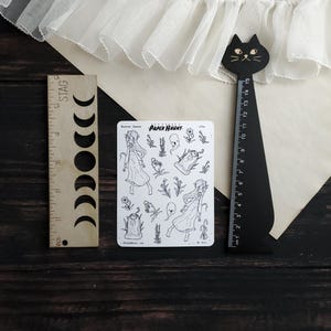 May include: A sheet of black and white stickers featuring a haunted garden theme. The stickers include a ghost, a tombstone, flowers, and two girls in dresses. The text "PAPER HAUNT." is printed on the sheet.