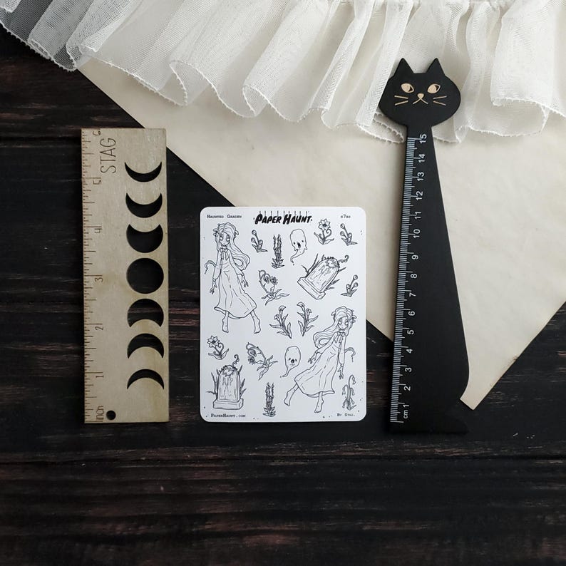 May include: A sheet of black and white stickers featuring a haunted garden theme. The stickers include a ghost, a tombstone, flowers, and two girls in dresses. The text "PAPER HAUNT." is printed on the sheet.