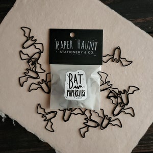 May include: A package of 12 black metal bat-shaped paperclips. The package is labeled "Bat Paperclips" and "Paper Haunt Stationery & Co."