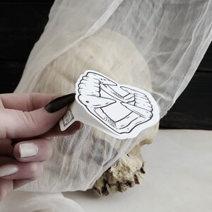 May include: A black and white sticker of a set of fangs, with a small star in the center. The sticker is placed on a white surface.
