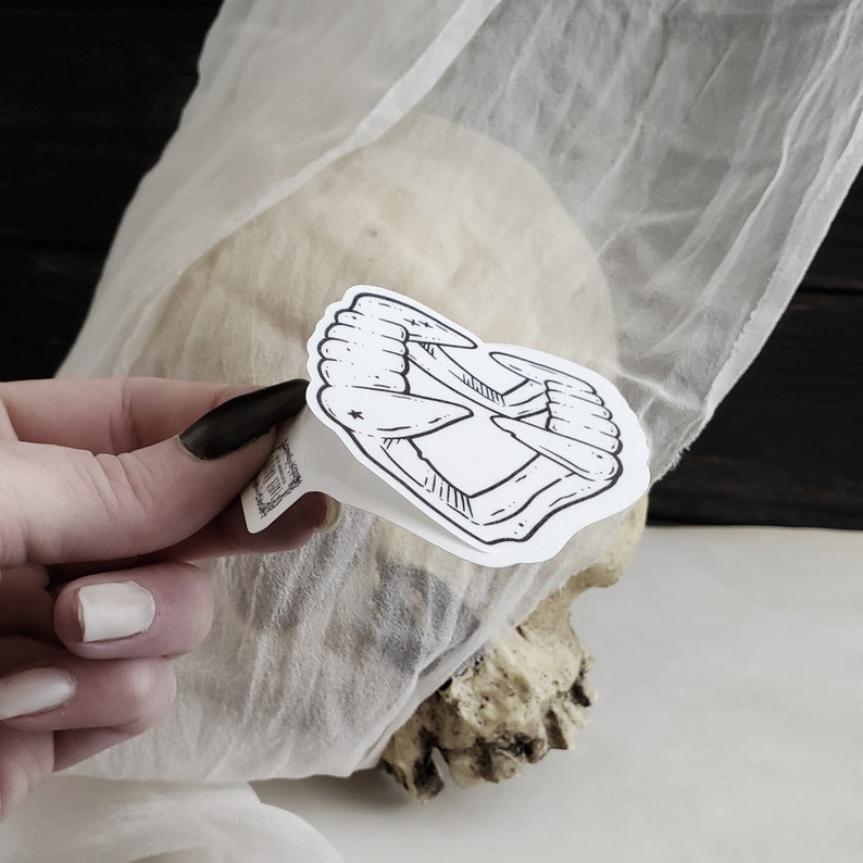 May include: A black and white sticker of a set of fangs, with a small star in the center. The sticker is placed on a white surface.