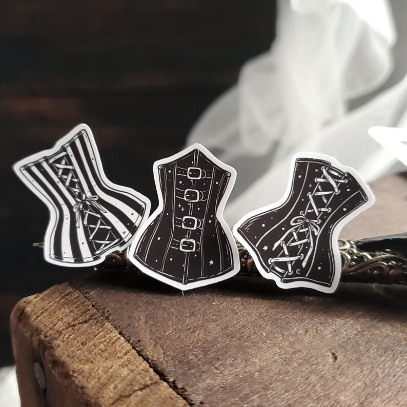 May include: Three black and white corset stickers with different designs. The corsets are decorated with stars and lace.