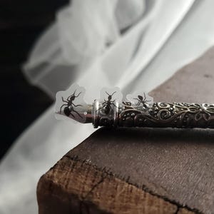May include: A silver pen with an ornate design and three clear stickers with black ant silhouettes on top.