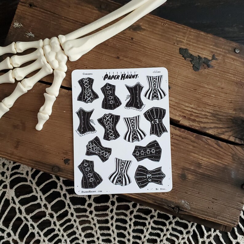 May include: A sheet of black and white stickers featuring various corset designs. The stickers are labeled "Corsets" and "Paper Haunt".