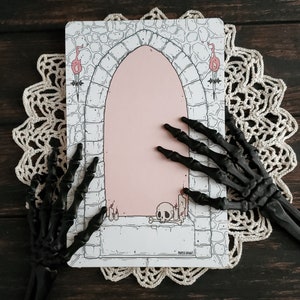 Pode incluir: Um cart&atilde;o imprim&iacute;vel com uma ilustra&ccedil;&atilde;o em preto e branco de um arco de pedra com um interior rosa. O arco &eacute; ladeado por duas tochas e uma caveira fica no ch&atilde;o abaixo. O texto "PAPER HAUNT" &eacute; impresso na parte inferior do cart&atilde;o.