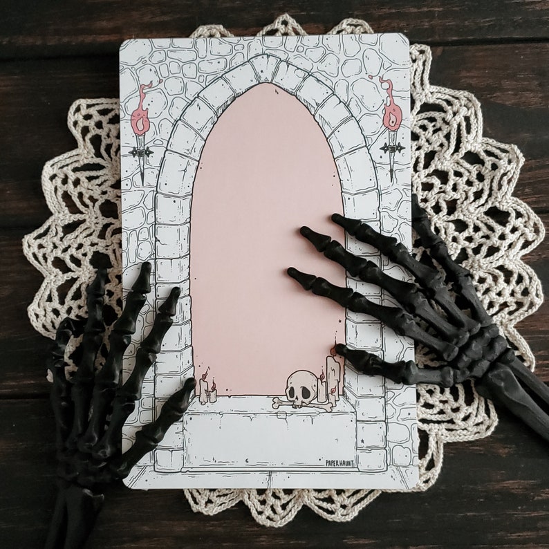 Pode incluir: Um cart&atilde;o imprim&iacute;vel com uma ilustra&ccedil;&atilde;o em preto e branco de um arco de pedra com um interior rosa. O arco &eacute; ladeado por duas tochas e uma caveira fica no ch&atilde;o abaixo. O texto "PAPER HAUNT" &eacute; impresso na parte inferior do cart&atilde;o.