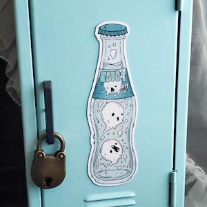 Può includere: Un adesivo raffigurante una bottiglia di soda "Ecto Pop" a cartoni animati con due personaggi simili a fantasmi all'interno. L'adesivo, con dettagli blu, è su un armadietto azzurro. Un lucchetto in ottone è appeso alla porta dell'armadietto.