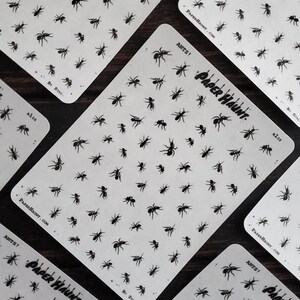 May include: A sheet of black ant stickers with the text "ANTS!" and "PAPER HAUNT" on it. The sheet is white with a subtle texture.