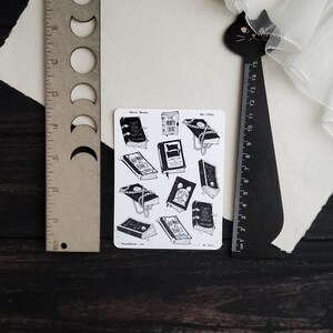 May include: A sheet of stickers featuring black and white illustrations of books with chains and the text "Ghost Stories", "The Time-Worn Library", and "A Scary Good Read".
