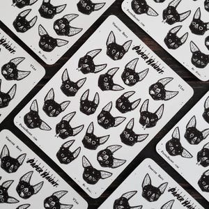 May include: A sheet of black and white stickers featuring vampire bats with various expressions. The stickers are printed on white paper with the text "Vampire Bats" and "Paper Haunt" in black.