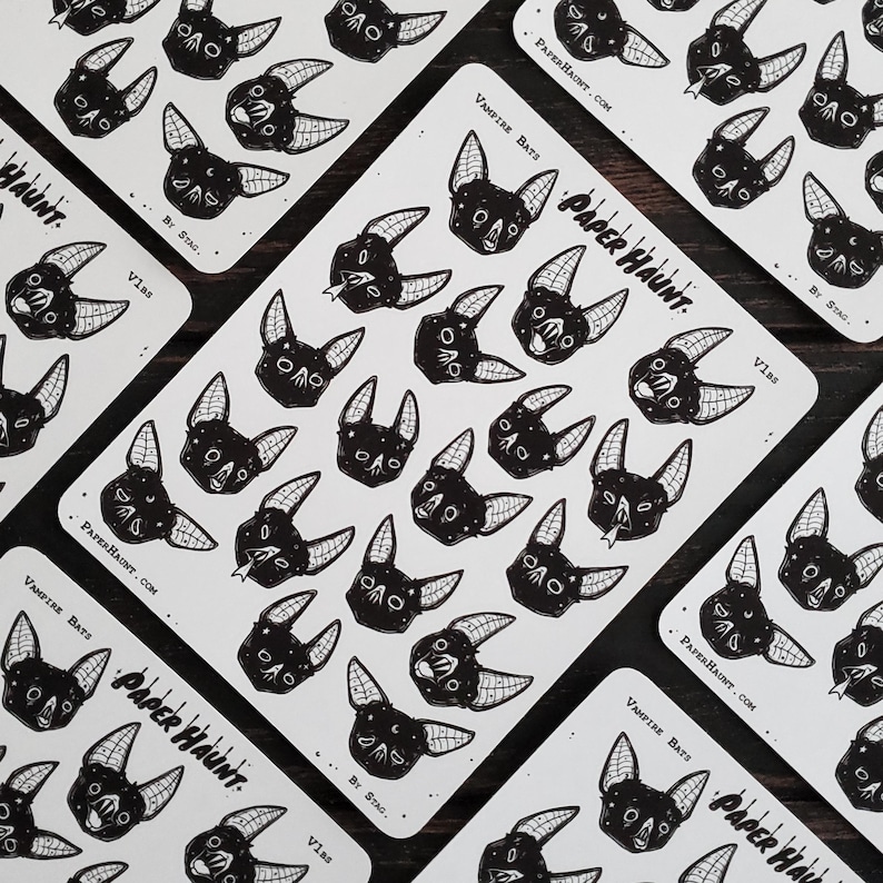May include: A sheet of black and white stickers featuring vampire bats with various expressions. The stickers are printed on white paper with the text "Vampire Bats" and "Paper Haunt" in black.