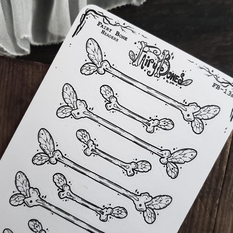 May include: A sheet of stickers featuring black and white illustrations of fairy bone headers. The stickers have a whimsical design with bone-shaped elements and leaf-like accents. The text "Fairy Bone Headers" and "Fairy Bones" are visible.