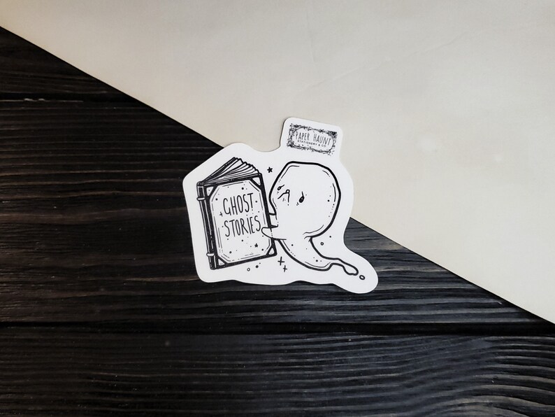 May include: A black and white sticker of a ghost reading a book that says "Ghost Stories".