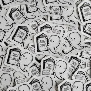 May include: A collection of black and white stickers featuring a ghost reading a book with the text "Ghost Stories".