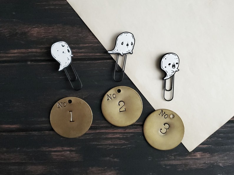 May include: Three brass bookmarks with ghost illustrations and black paper clips. The bookmarks are numbered "No. 1", "No. 2", and "No. 3".