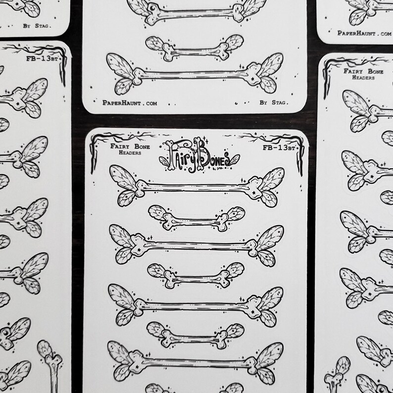 May include: A collection of white stickers featuring black illustrations of fairy bones. The stickers have a bone-like shape with leaf-like details at the ends. The text "Fairy Bones" and "FB-13BT" is visible on the stickers. The website "PAPERHAUNT.COM" is also visible.