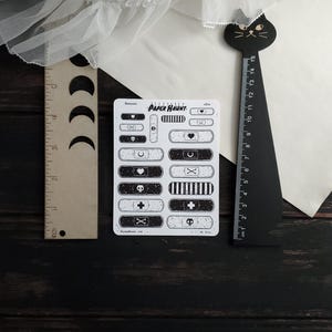 May include: A sheet of black and white patterned bandaid stickers. The stickers feature various designs including hearts, skulls, crosses, and crescent moons. The sheet is labeled "PAPER HAUNT".