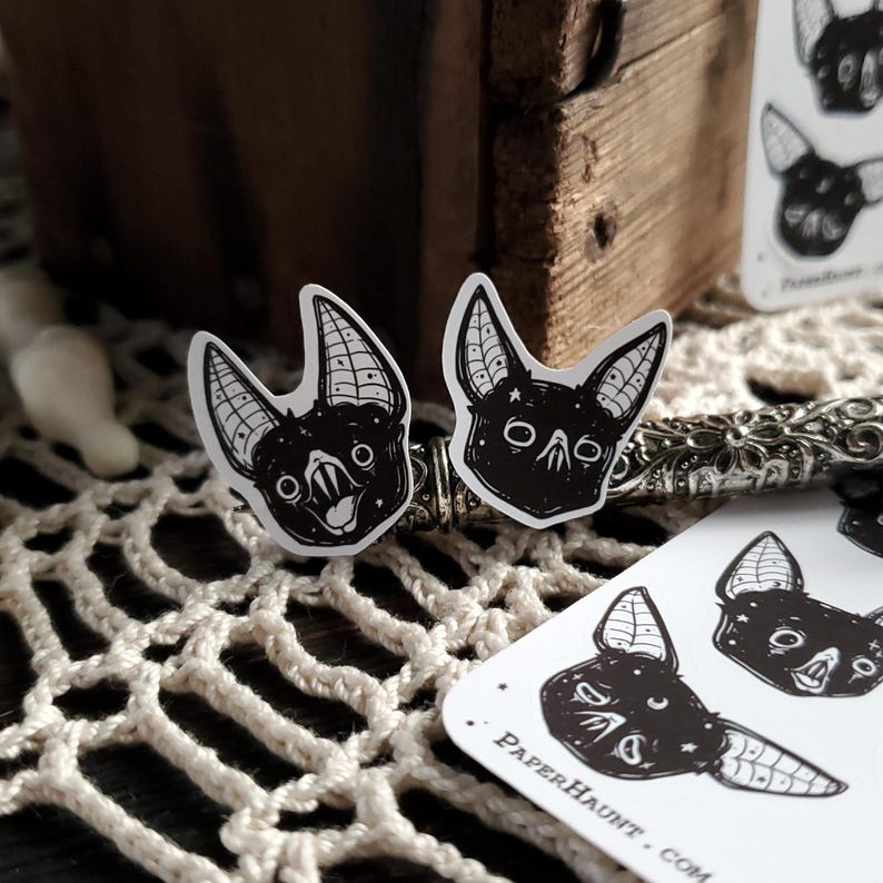 May include: Two black and white bat stickers with detailed wings and eyes. The stickers are on a white background with the text "PaperHaunt.com" in the bottom right corner.