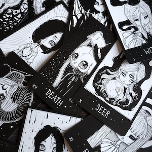 May include: A set of black and white tarot cards with illustrations of various characters. The cards feature a skull with an axe, a woman with a crystal ball, and a woman with a star. The cards are labeled with the names of the tarot cards, such as "Death" and "Seer".