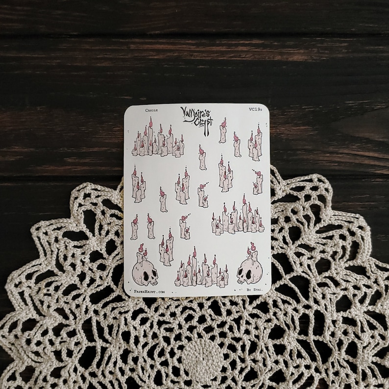 May include: A sheet of stickers featuring a variety of white candles with pink flames. The stickers are on a white background and include two skull designs with the text "Vampire's Crypt".