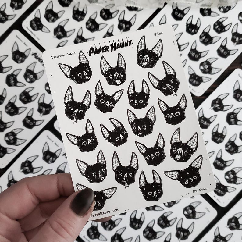 May include: A sheet of stickers featuring black and white illustrations of bats with various expressions. The stickers are arranged in a grid pattern and have a white background. The sheet is labeled "Vampire Bats" and "Paper Haunt."