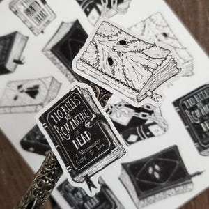 May include: A set of black and white stickers featuring illustrations of books. One sticker features a book with the title "110 Rules for Romancing the Dead: A Necromancer's Guide to Love."