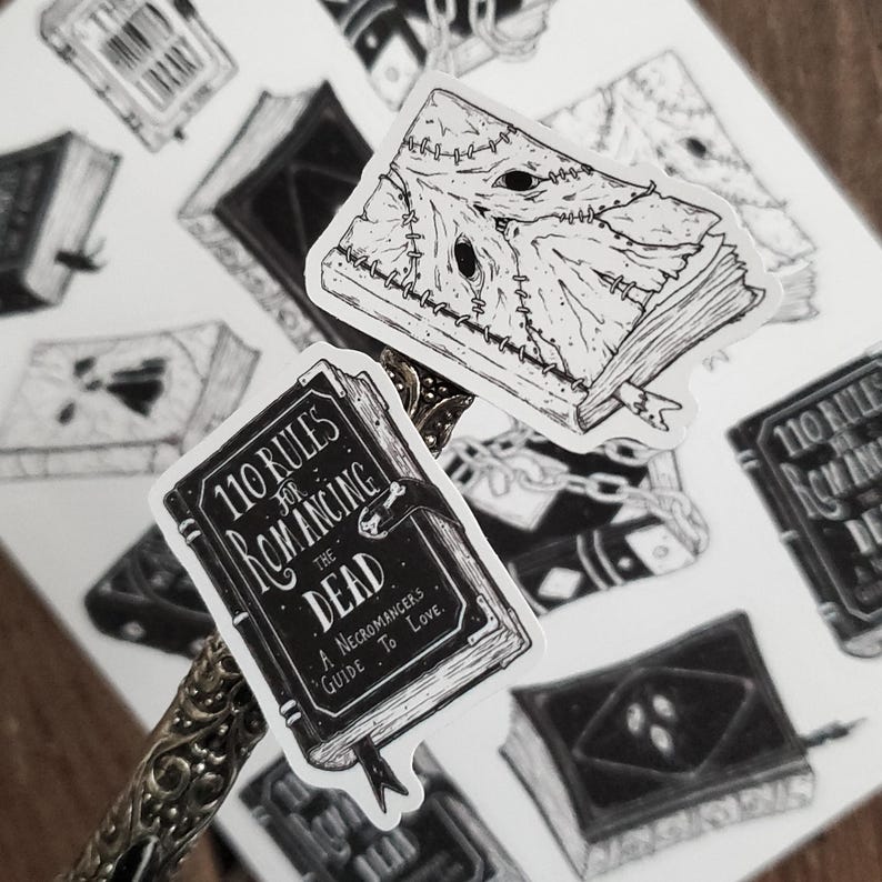 May include: A set of black and white stickers featuring illustrations of books. One sticker features a book with the title "110 Rules for Romancing the Dead: A Necromancer's Guide to Love."
