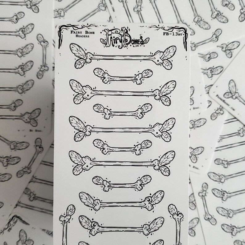 May include: A sheet of black and white stickers featuring stylized bone designs with leaf-like accents. The text "Fairy Bone Headers" and "Fairy Bones" is visible. The stickers are arranged in rows, with additional stickers scattered around.