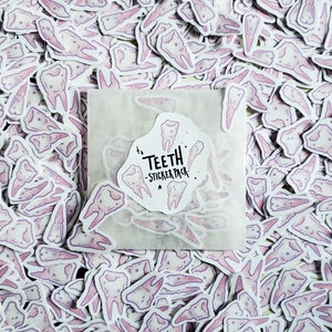May include: A white envelope containing a sticker pack of pink and purple tooth illustrations. The sticker pack is labelled "Teeth - Sticker Pack".