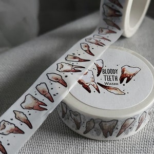 May include: A roll of white washi tape with a repeating pattern of brown teeth. The tape is labeled "Bloody Teeth Washi".