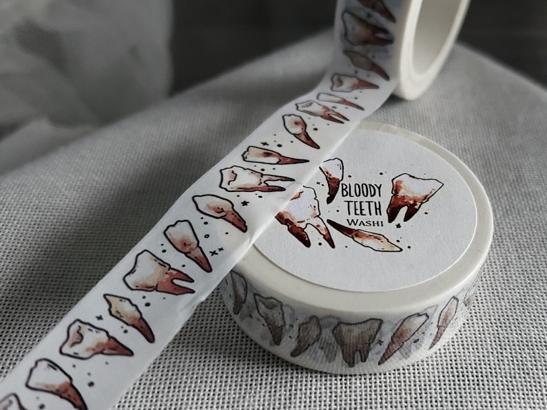 May include: A roll of white washi tape with a repeating pattern of brown teeth. The tape is labeled "Bloody Teeth Washi".