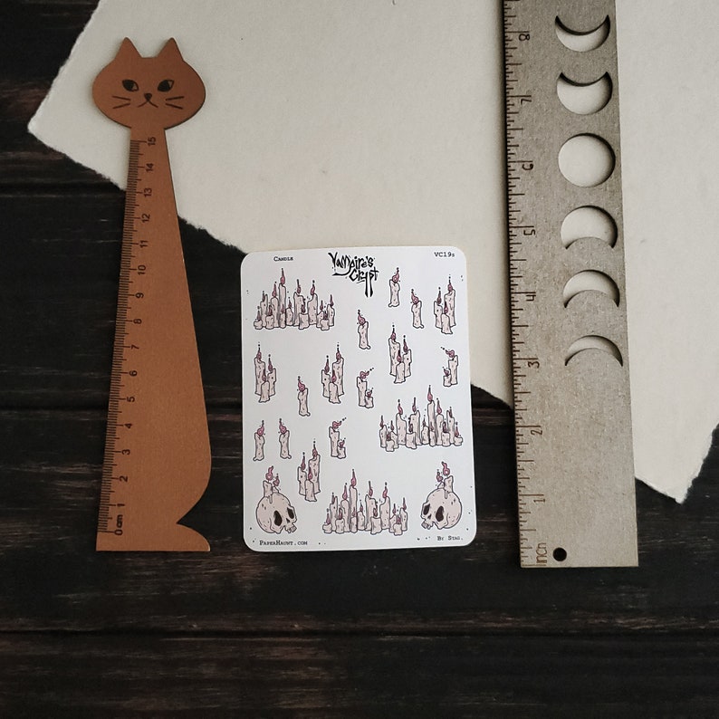 May include: A sheet of stickers featuring a variety of illustrations of candles and skulls. The stickers are white with black outlines and pink accents. The text "Yajaira's Craft" is printed in black at the top of the sheet.