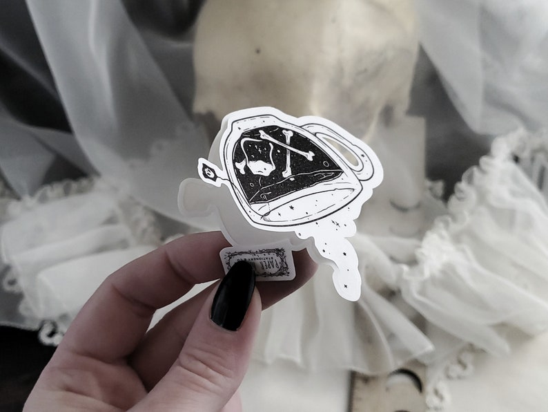 Op de afbeelding: Een zwart-witte sticker van een theepot met een schedel en gekruiste beenderen erin. De theepot giet een stroom stippen uit.