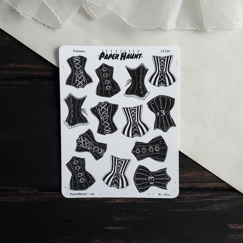 May include: A sheet of black and white stickers featuring various corset designs. The stickers are labeled "Corsets" and "Cillas" and feature the text "Paper Haunt."