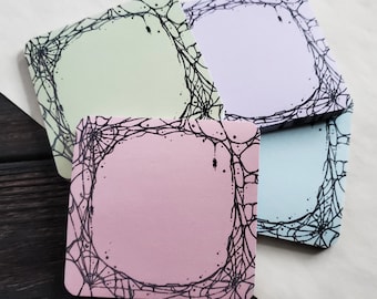 May include: Four square sticky notes with a black spiderweb design border. The notes are in pastel colors: light green, pink, light blue, and lavender.