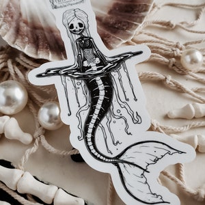 Close up of Spooky cute goth Jelly bones mermaid skeleton emerging from water, a sticker Featuring a Mermaid with Translucent skin with visible skeleton and organs with sea shell, fishing net and pearls.