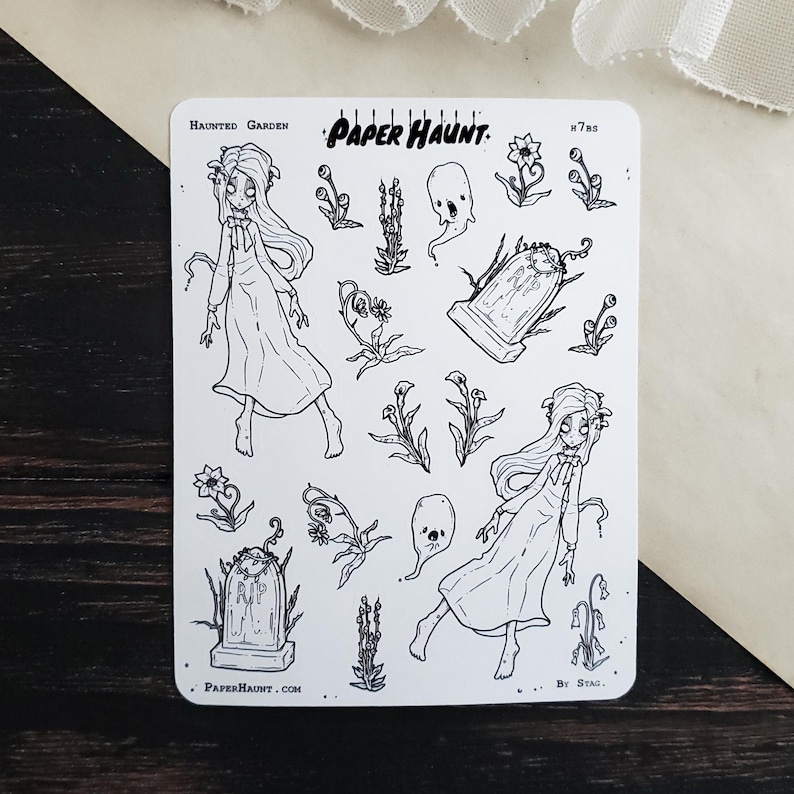 May include: A sheet of black and white stickers featuring a haunted garden theme. The stickers include two ghosts, two girls in dresses, a tombstone, and various plants. The sheet is titled "Haunted Garden" and "Paper Haunt."