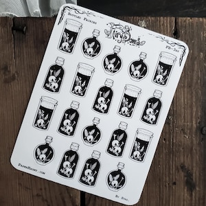 May include: A sheet of stickers featuring various black and white illustrations of bottled fairies. The designs include bottles and jars with skull and crossbones, and plant-like elements. The text "Bottled Fairies" and "Fairy Bones" are visible.