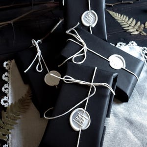 May include: Four black gift boxes tied with twine and sealed with white wax seals. Each seal has a different design, including a floral pattern and the text "Made with Love".